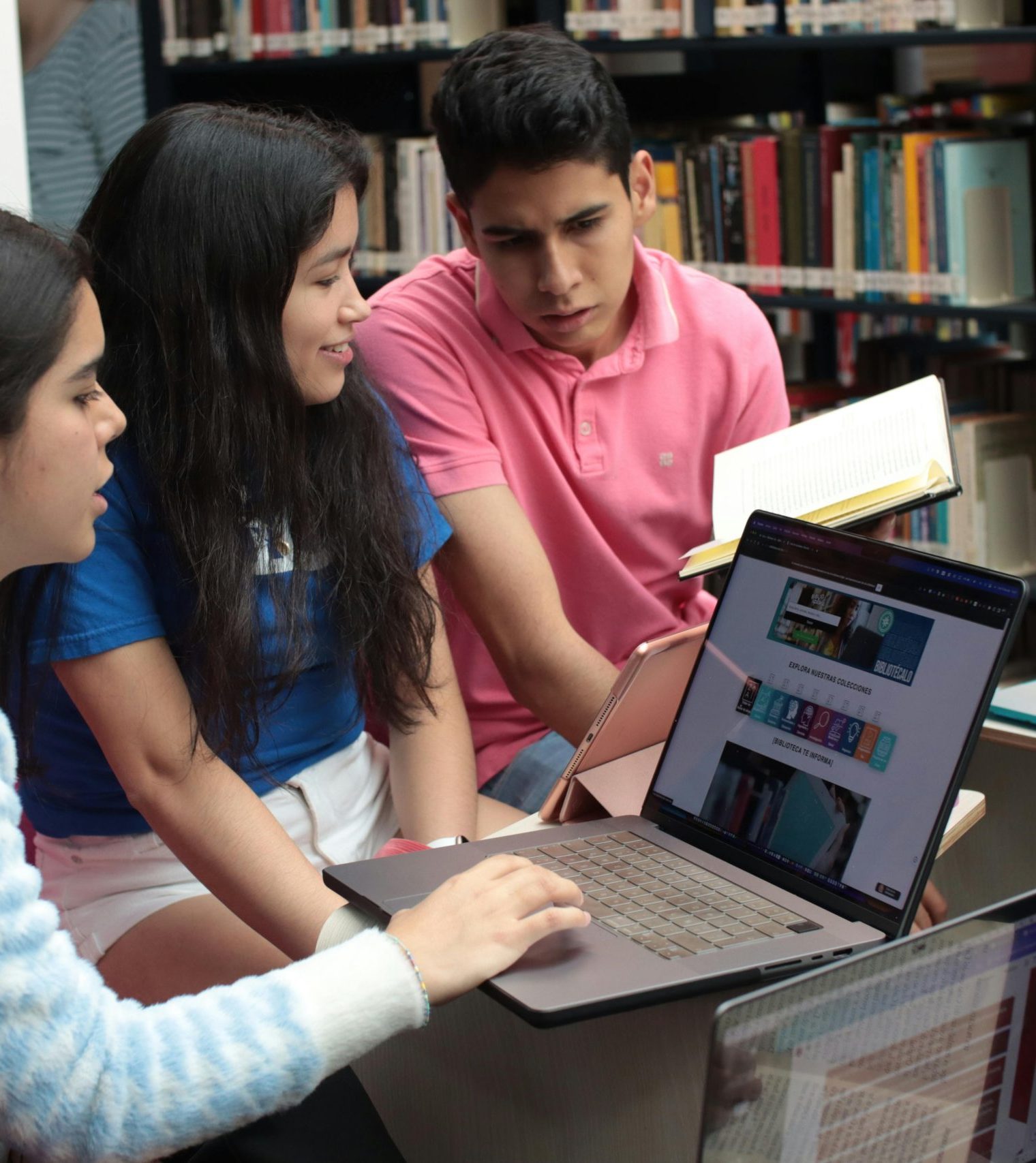 Group of young students studying and discussing in a library setting with books and laptops.